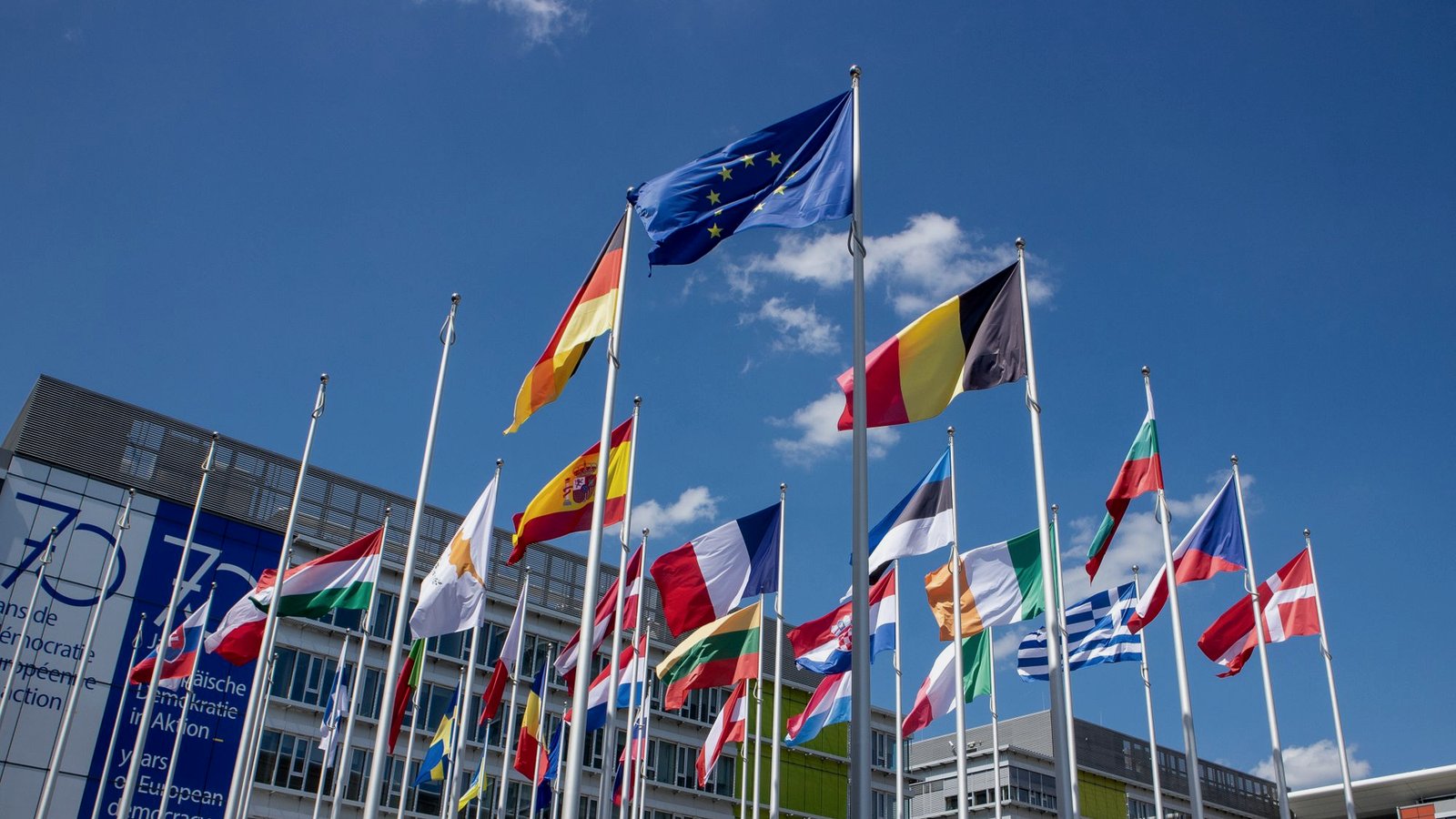 Low-angle view of European Union flags on flagpoles against a clear blue sky.
