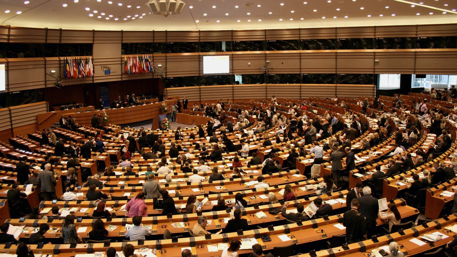 Wide interior view of the European Parliament plenary chamber in Brussels with members of parliament seated in concentric tiers around the speaker's podium.