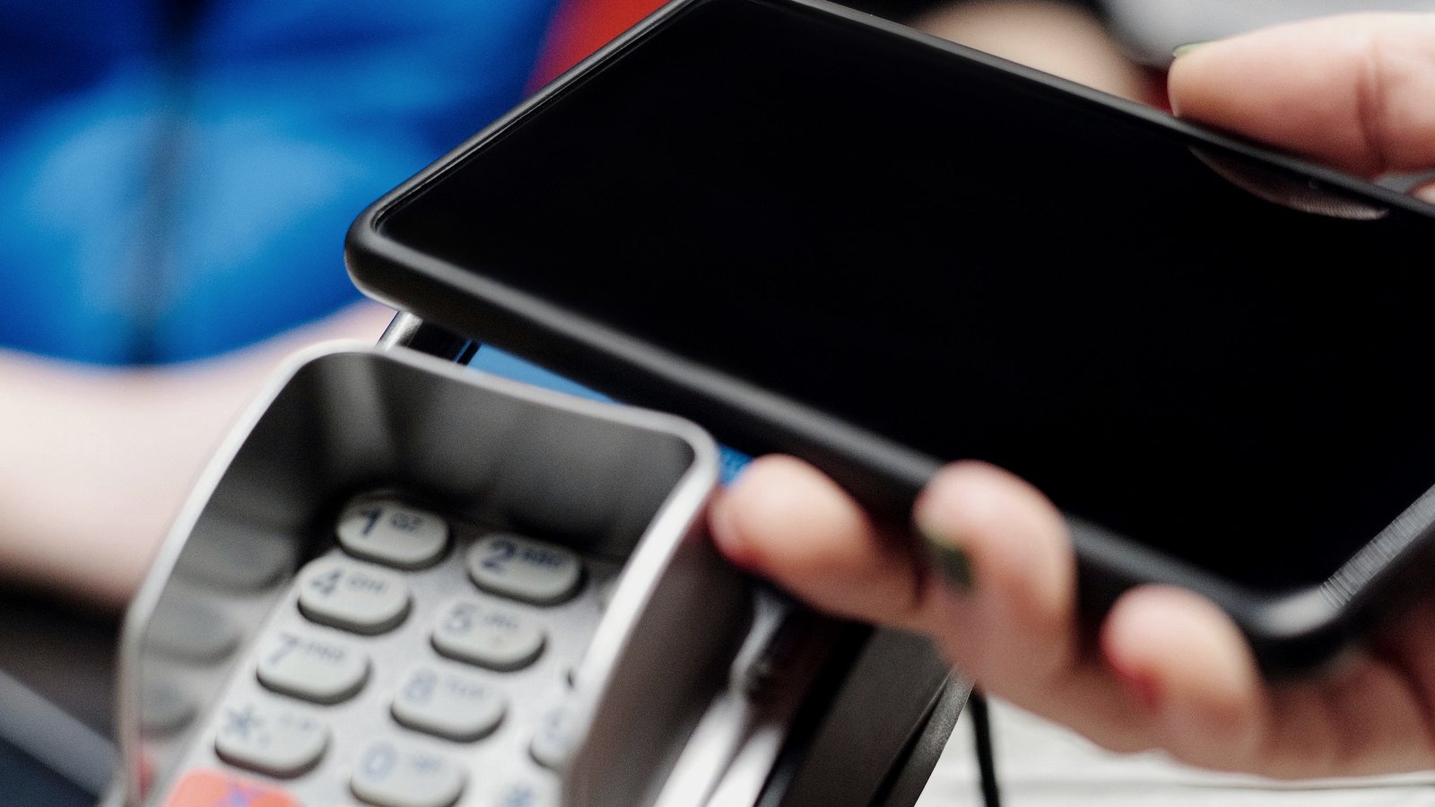 A customer holds a smartphone above a contactless payment terminal.